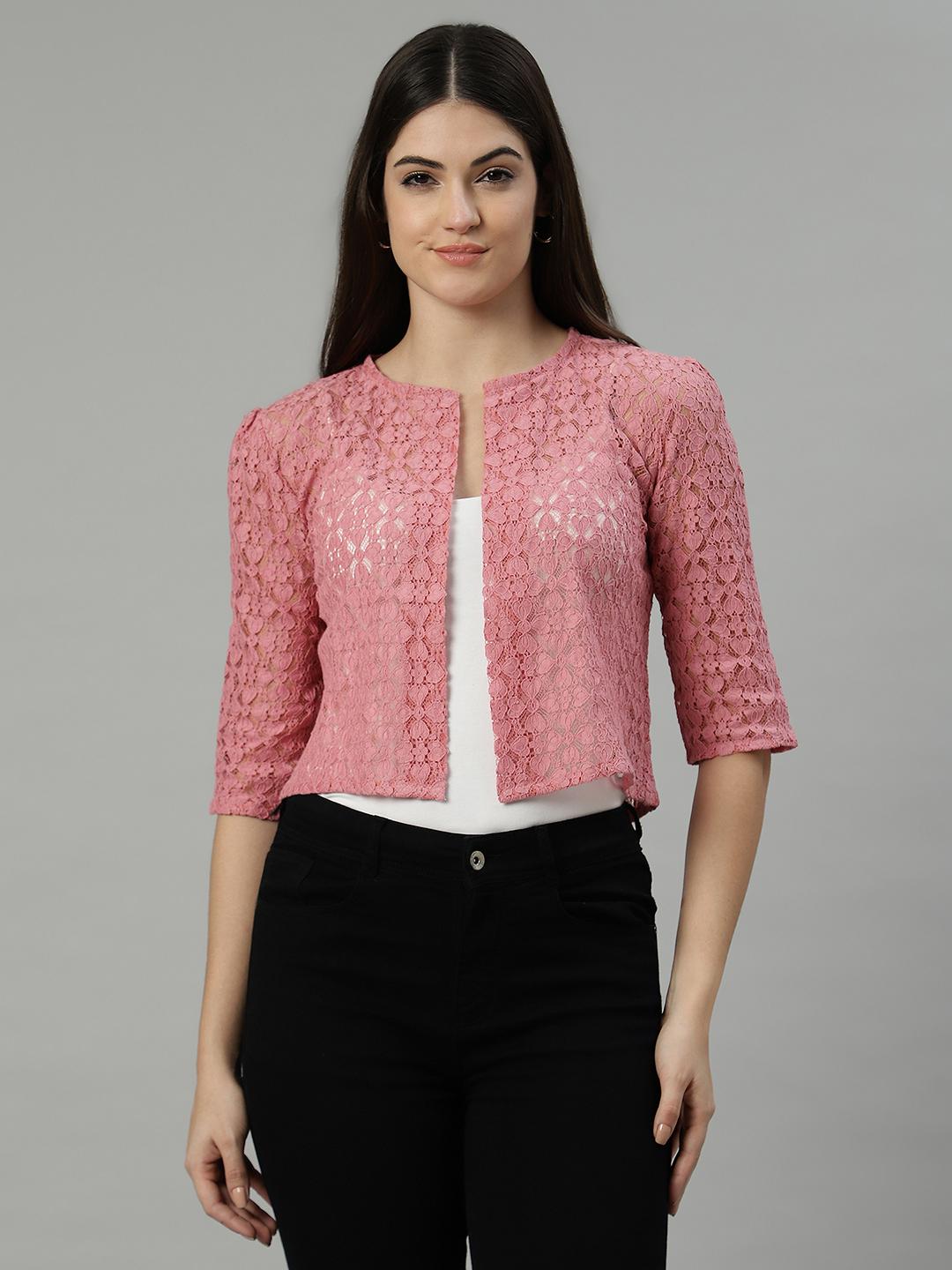 Woman wearing a peach textured shrug over a white top and black pants on a gray background