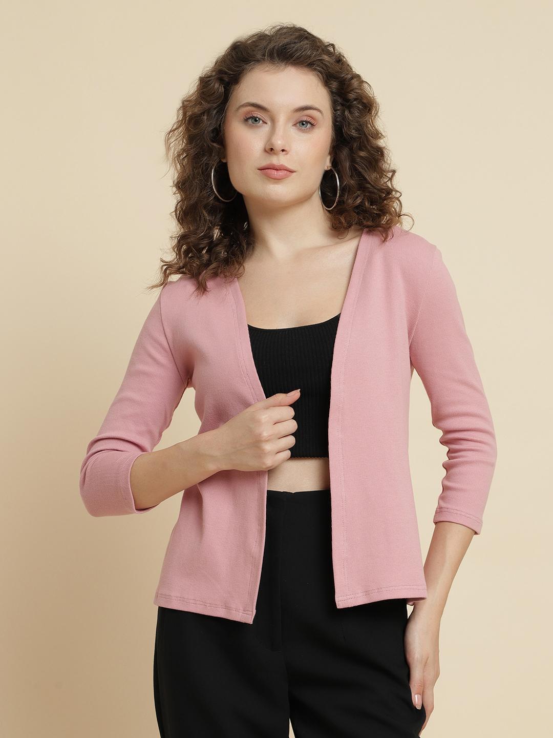 Woman wearing a pink cardigan over a black top and pants on a beige background