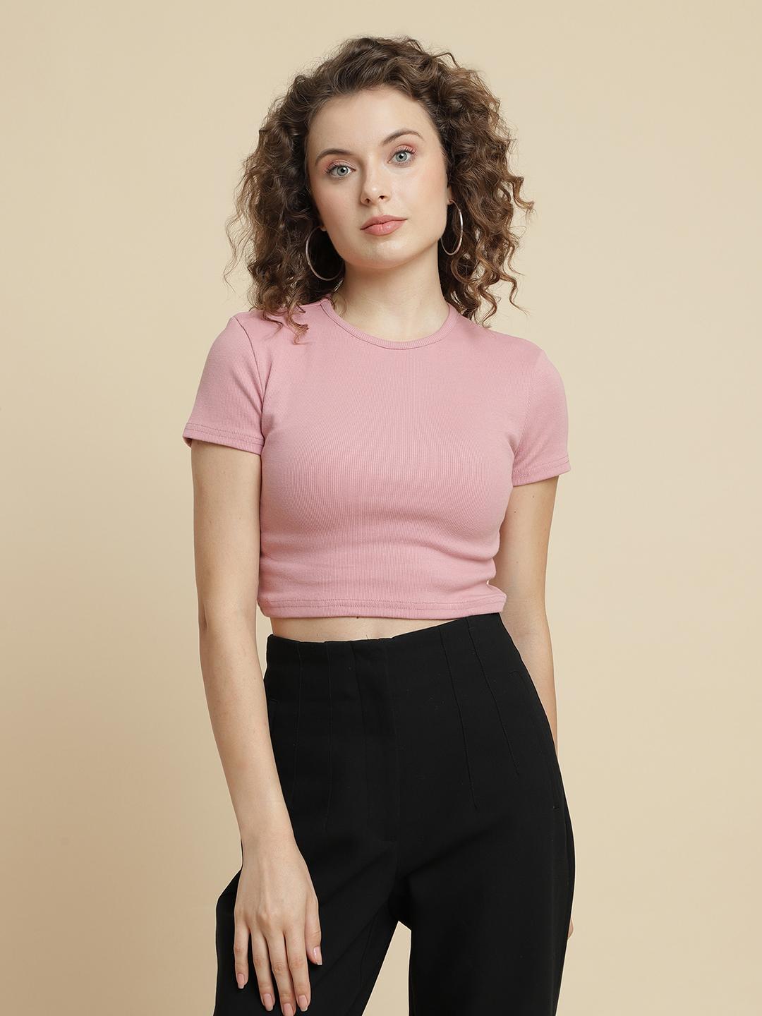 Woman wearing a pink crop top and black pants against a beige background