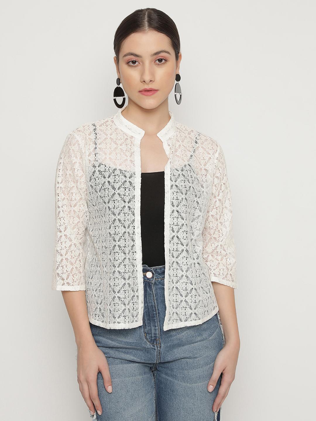 Woman wearing a white lace shrug over a black shirt with blue jeans on a light gray background