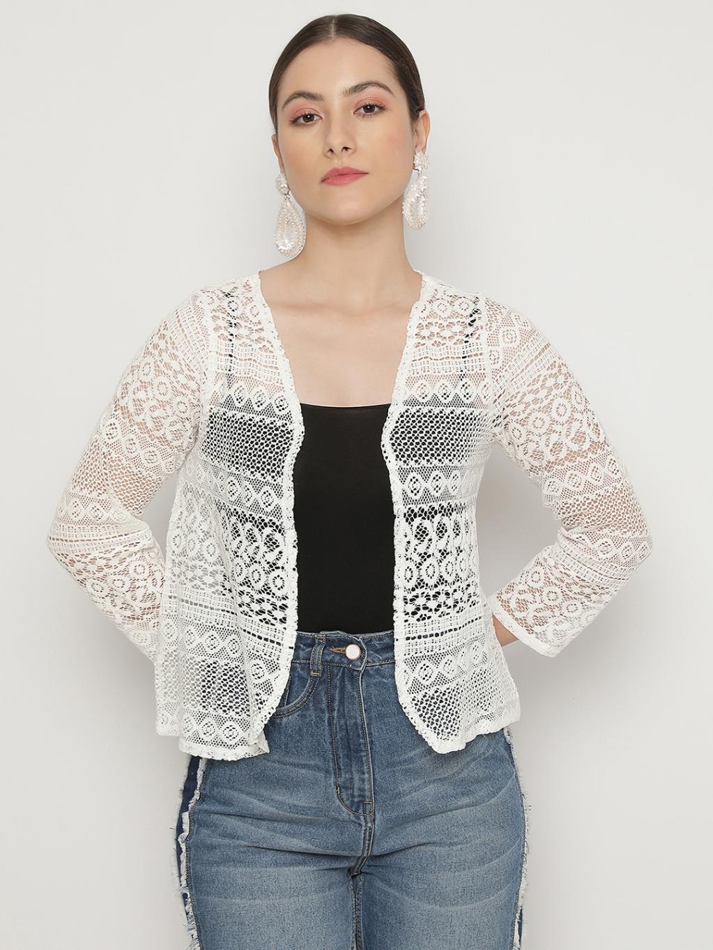 Woman wearing a white lace cardigan over a black top and blue jeans on a white background