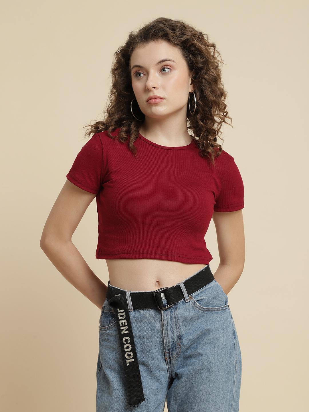 Woman wearing a red crop top and blue jeans with a beige background