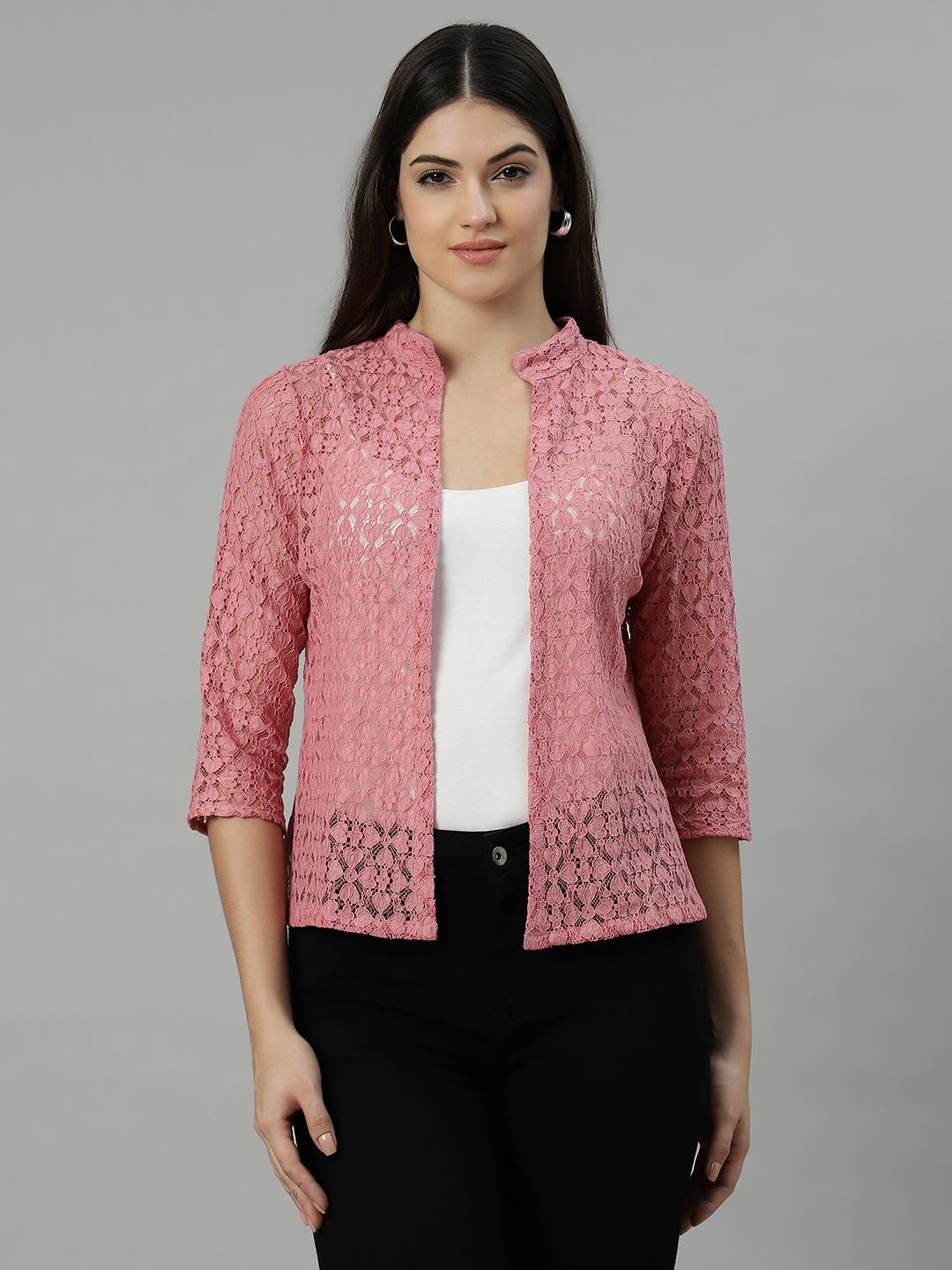 Woman wearing a pink lace shrug over a white top and black pants on a gray background