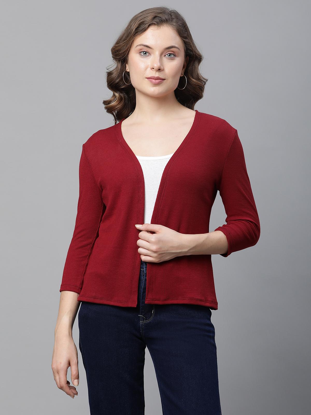 Woman wearing a red cardigan over a white shirt and dark jeans on a gray background