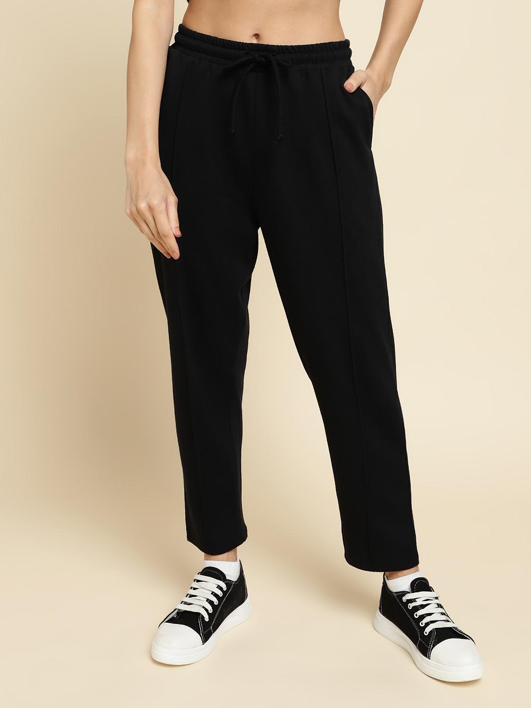 Person wearing black jogger pants and black sneakers on a beige background