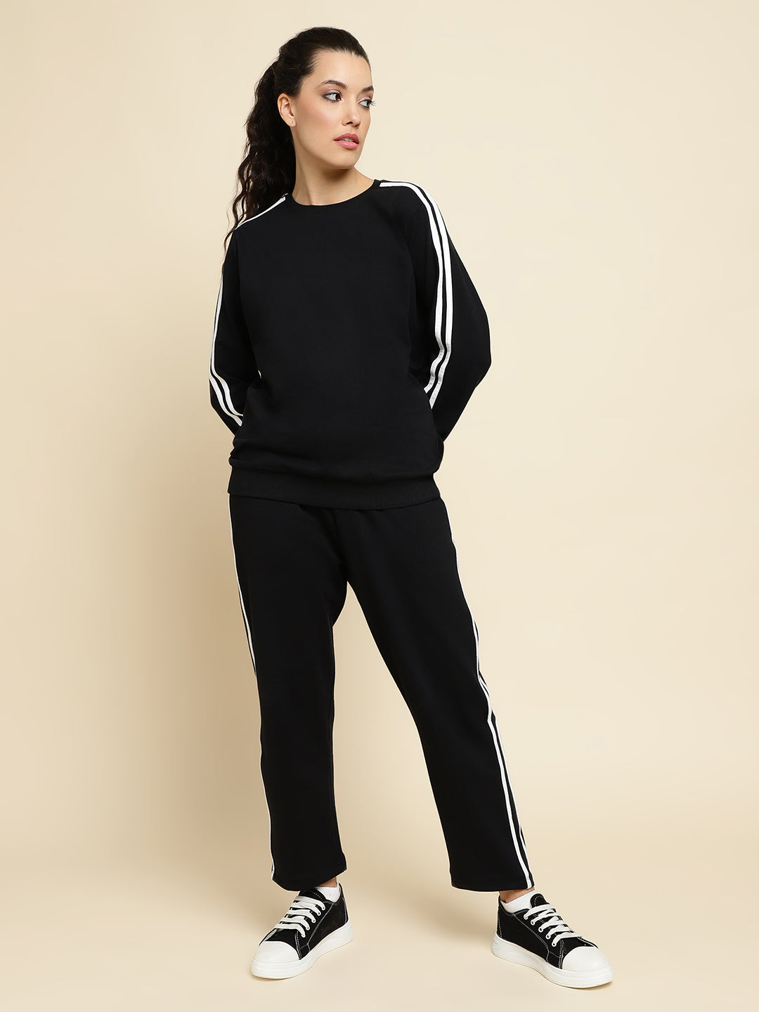Woman wearing a black tracksuit with white stripes on a beige background