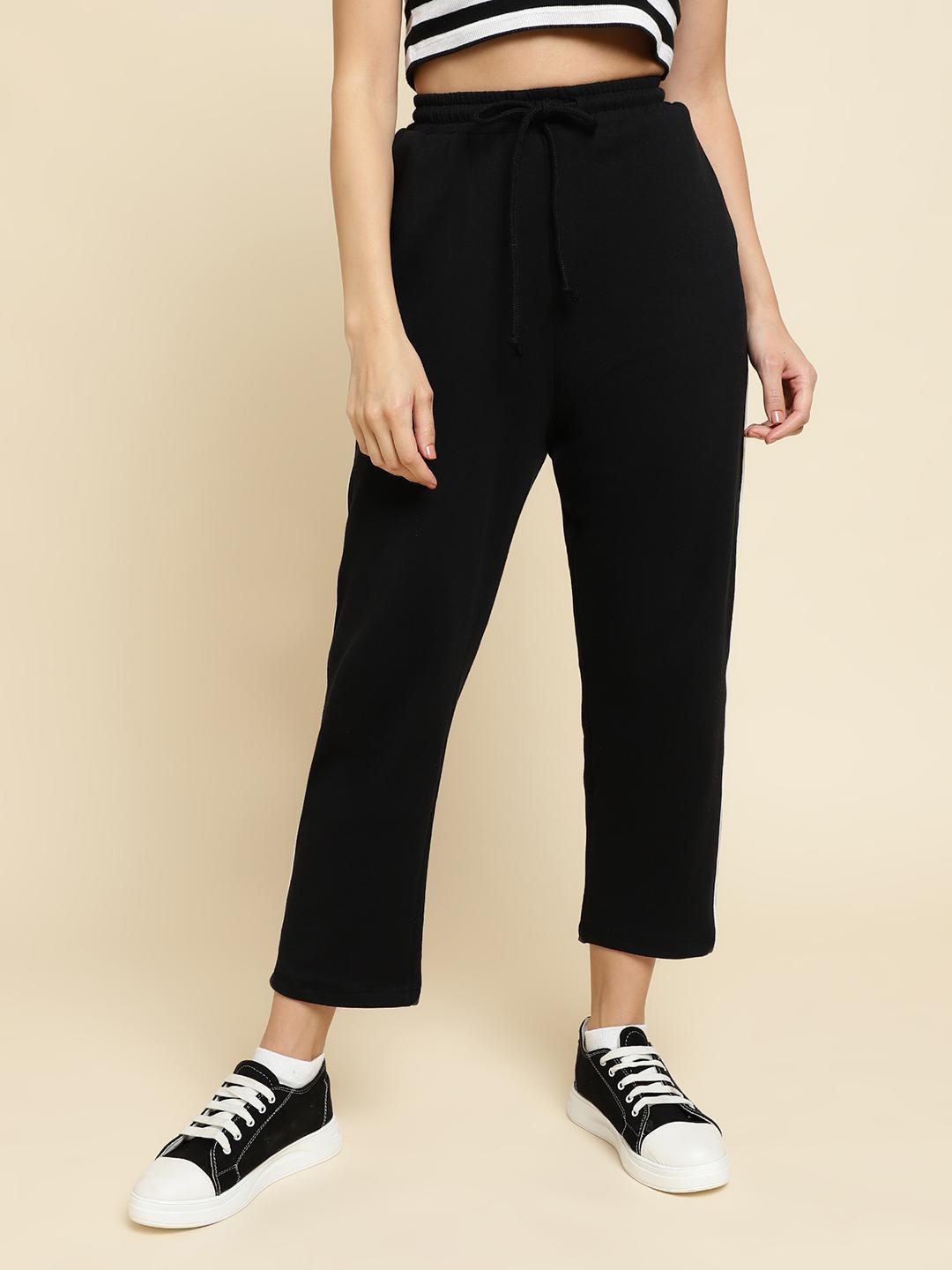 Person wearing black pants and black and white sneakers on a beige background