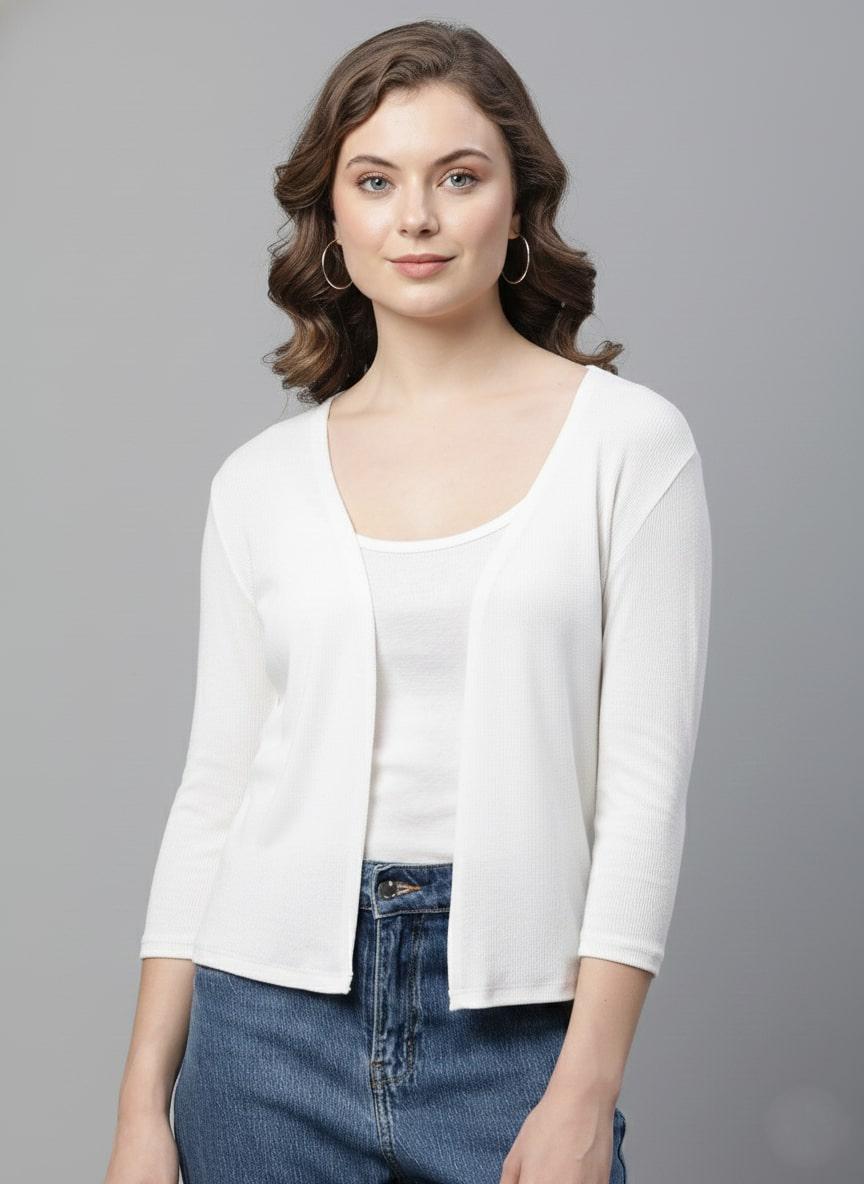 Woman wearing a white shrug over a white shirt with blue jeans on a gray background