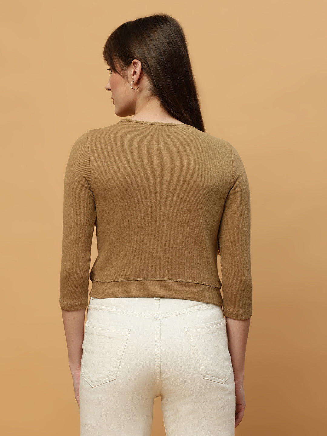 Woman wearing a brown long-sleeve top and white pants against a beige background