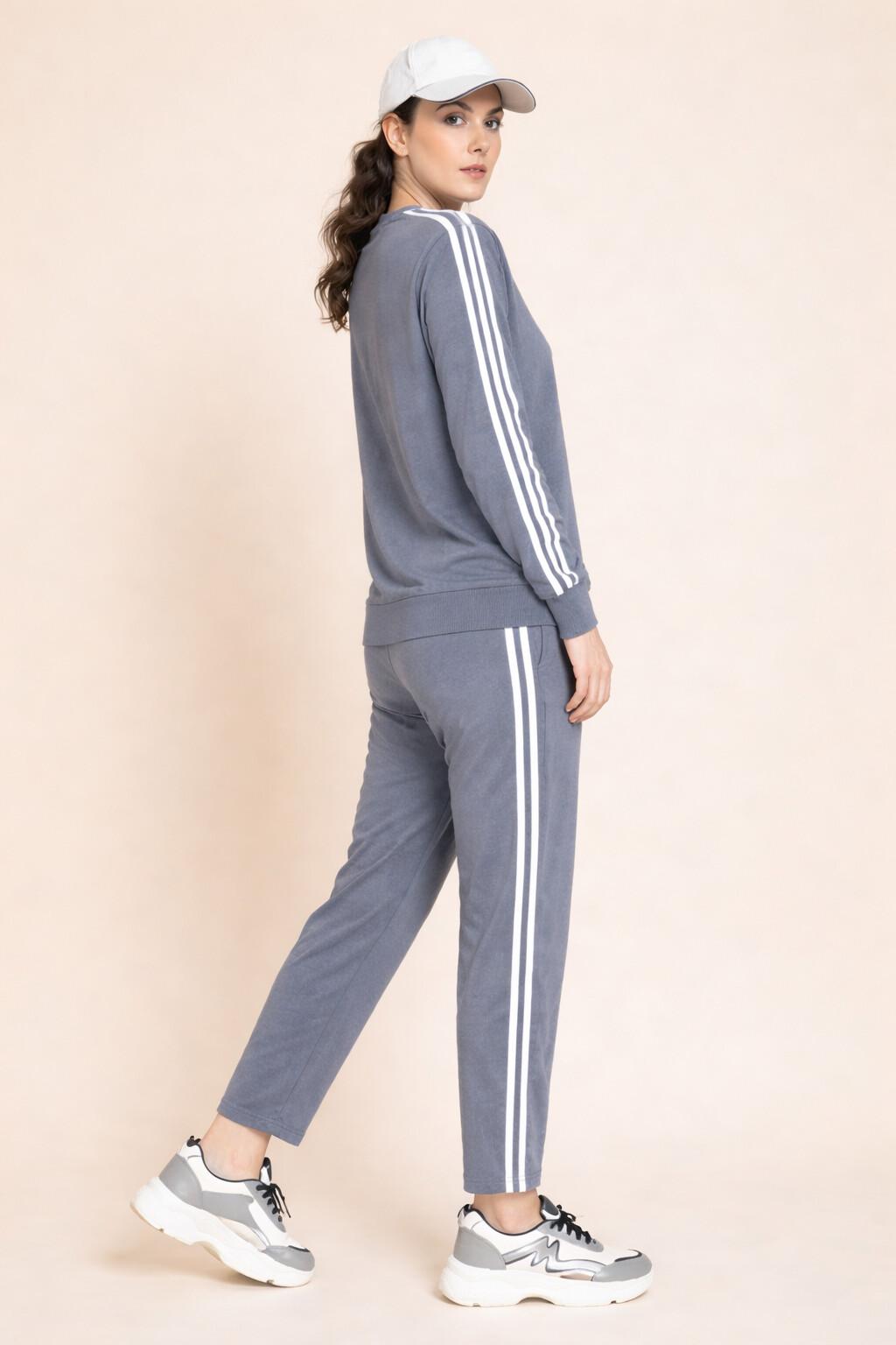 Woman wearing a gray tracksuit with white stripes on a beige background