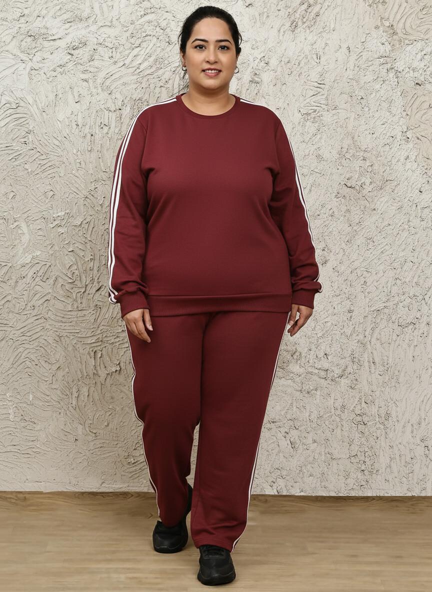 Person wearing a maroon tracksuit with white stripes against a textured wall.