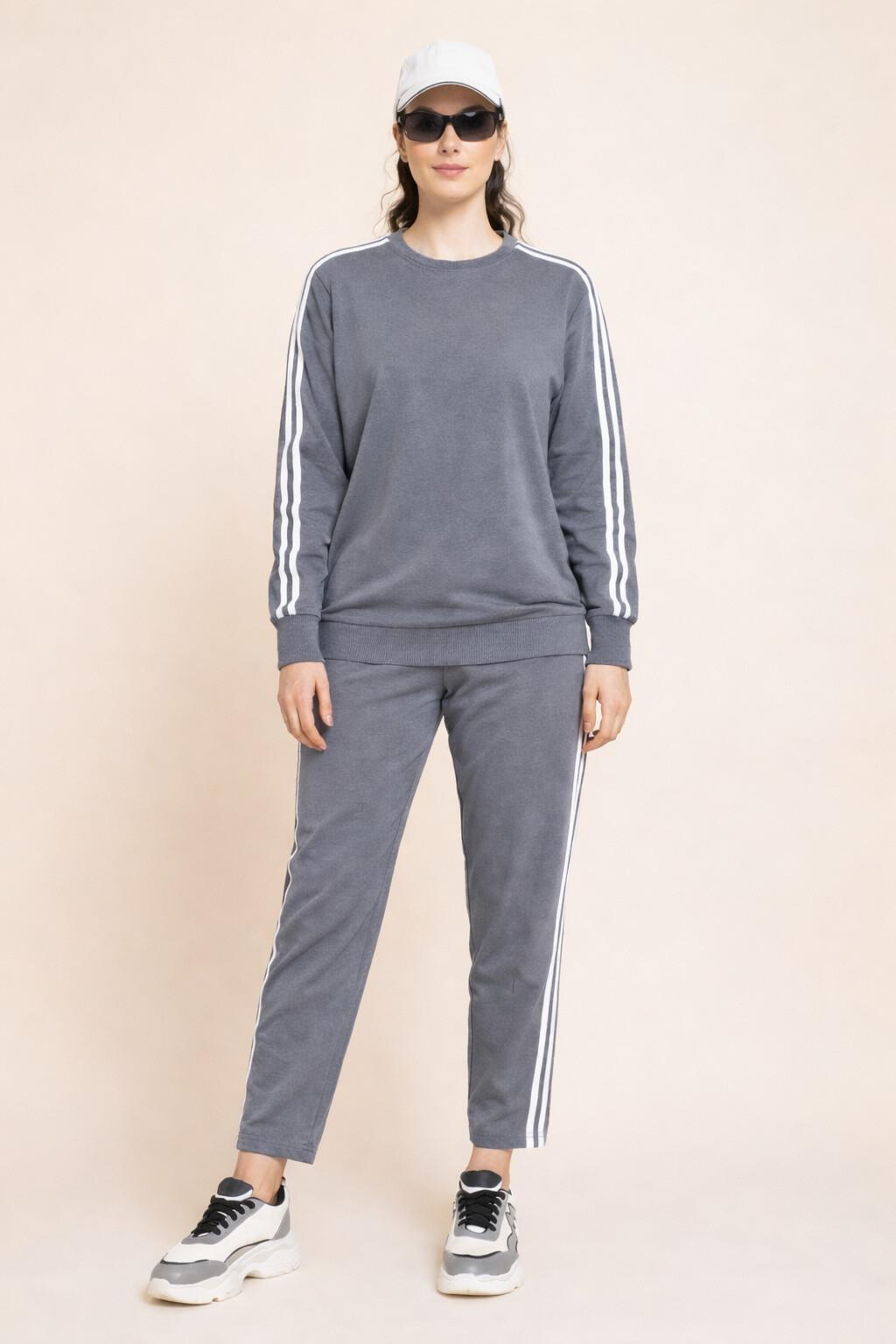 Person wearing a gray tracksuit orco-ords set with white stripes on a beige background