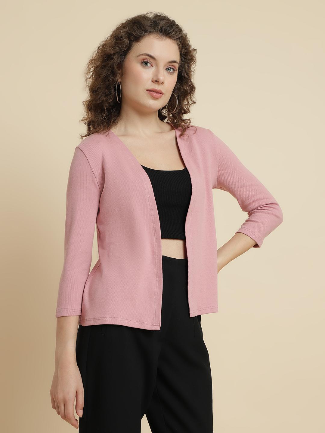 Woman wearing a pink shrug over a black top and pants on a beige background
