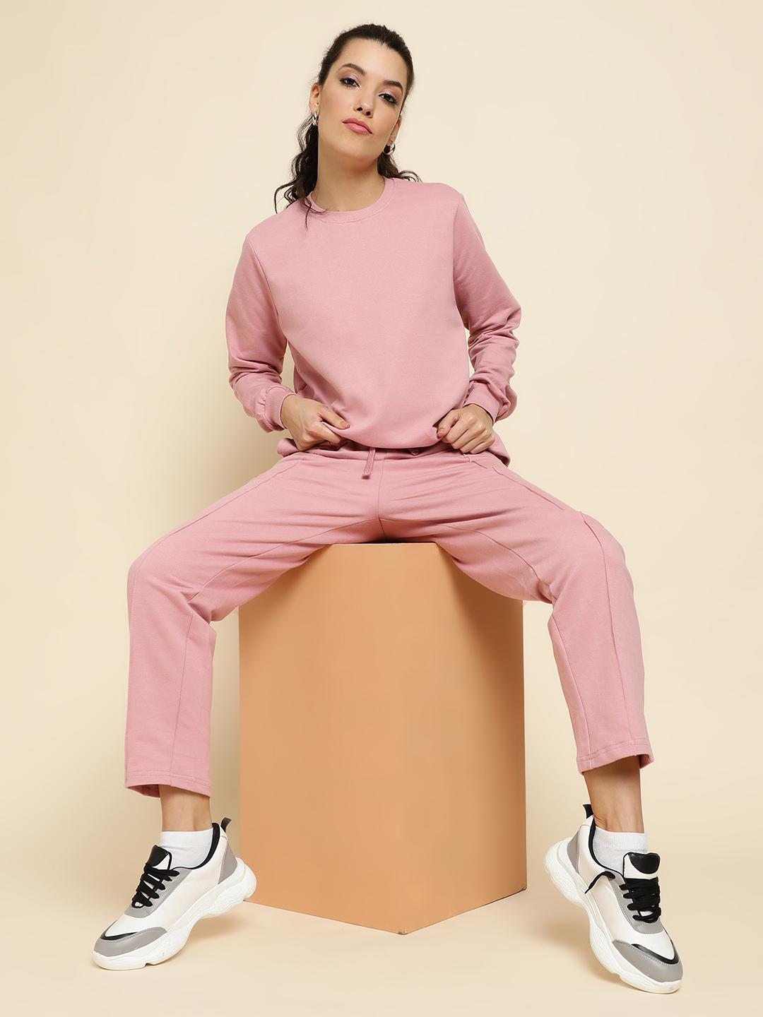 Woman wearing a peach tracksuit sitting on a beige cube against a beige background
