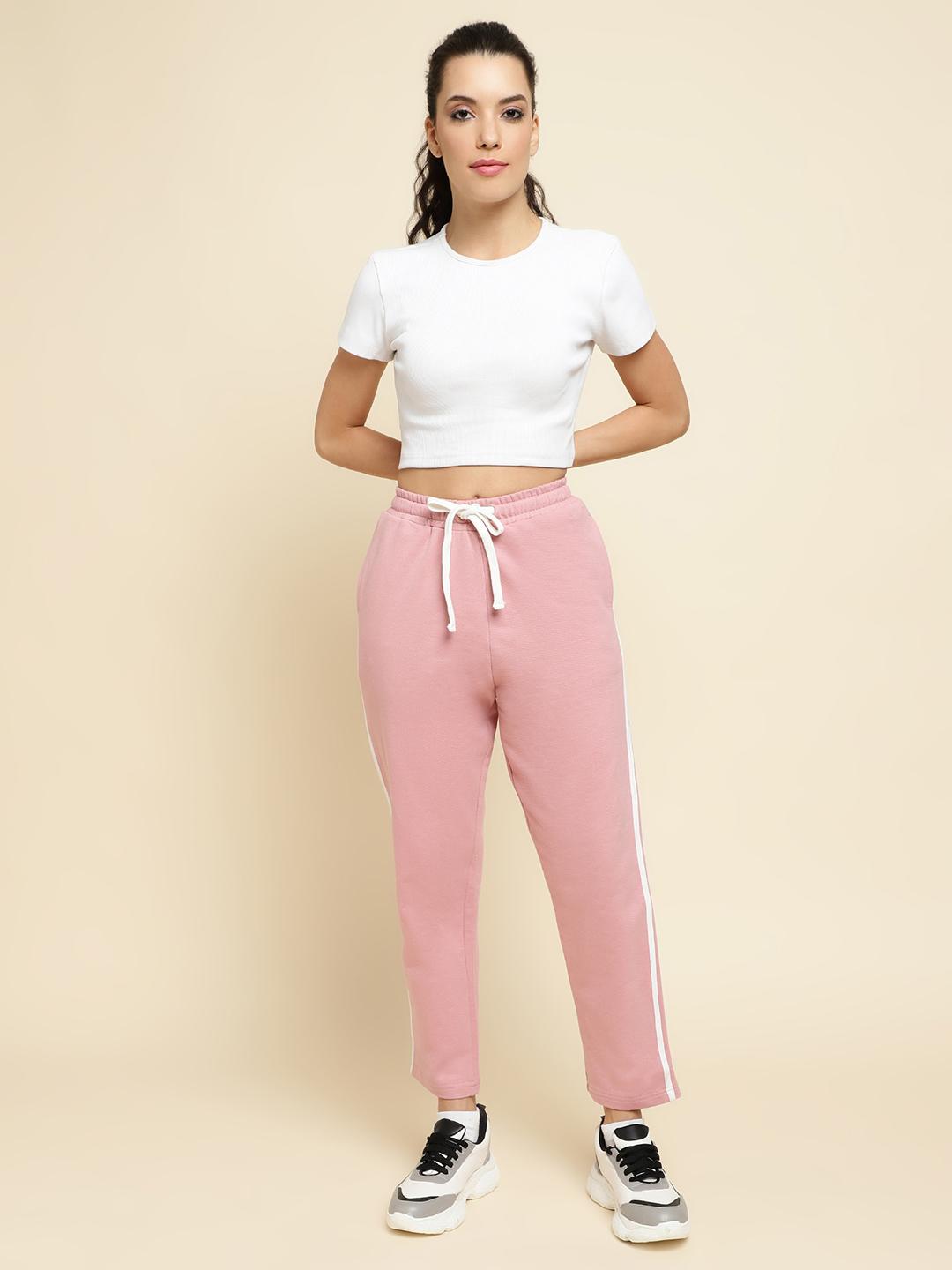 Woman wearing a white crop top and peach sweatpants with a beige background