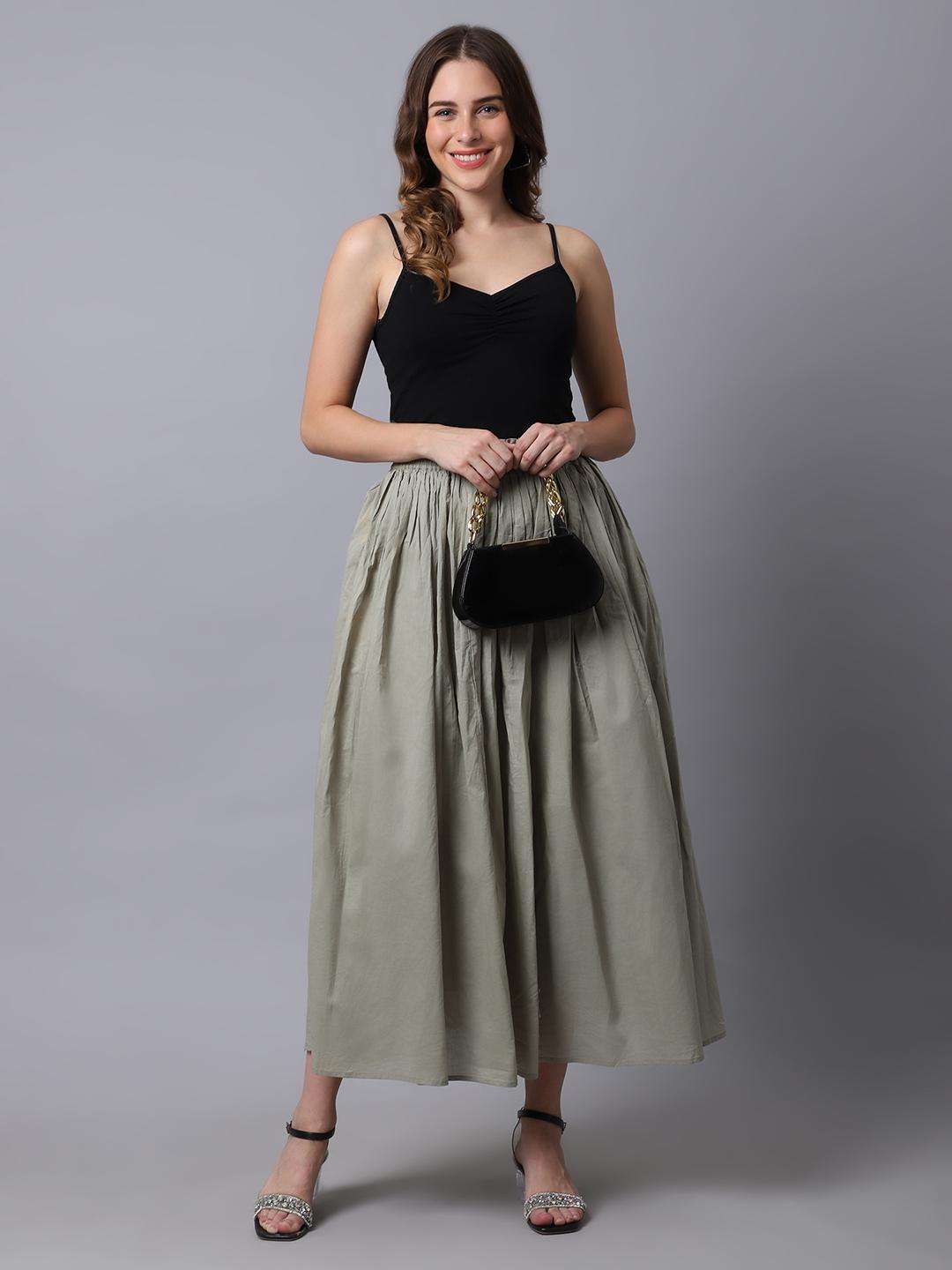 Woman wearing a black top and green skirt holding a black handbag against a gray background