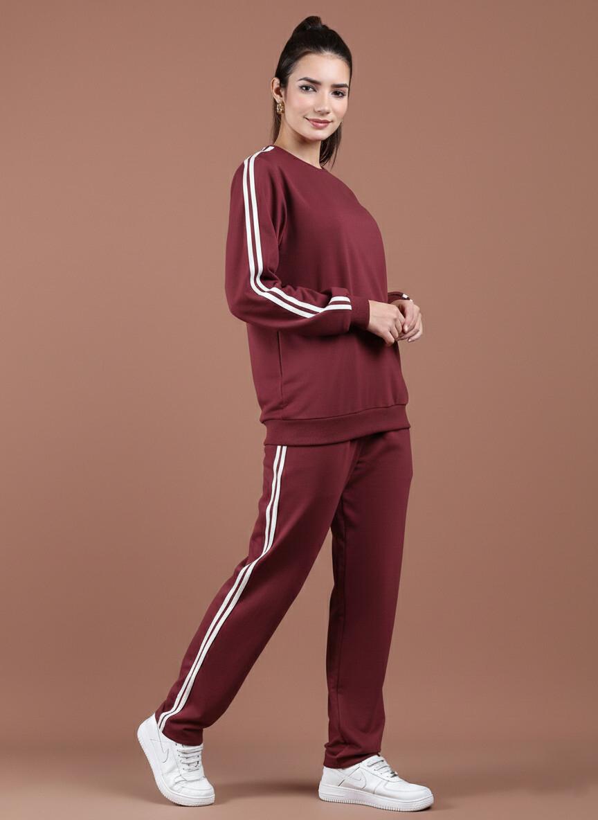 Woman wearing a maroon tracksuit with white stripes on a brown background
