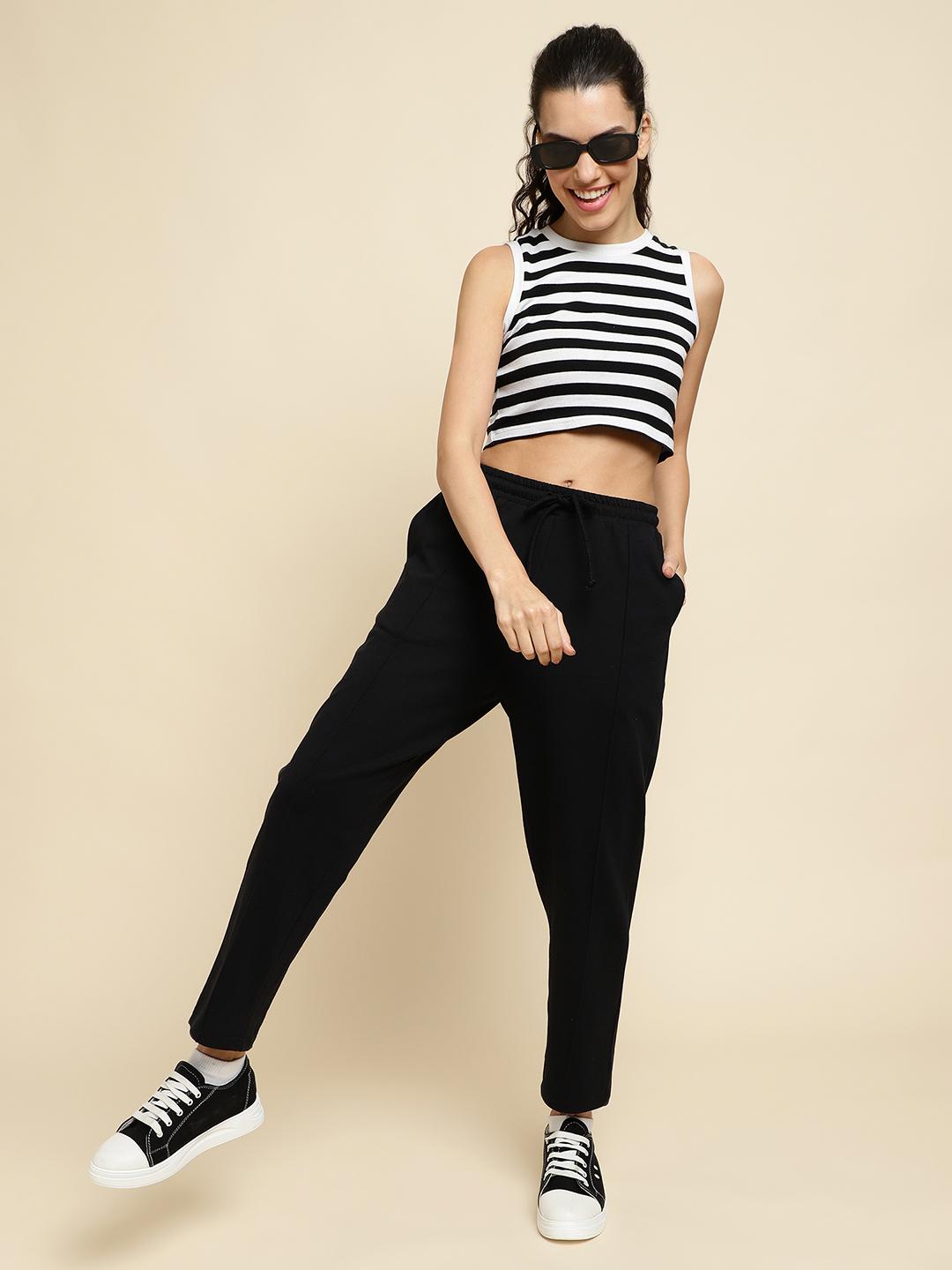 Woman wearing a black and white striped sleeveless top and black track pants on a beige background