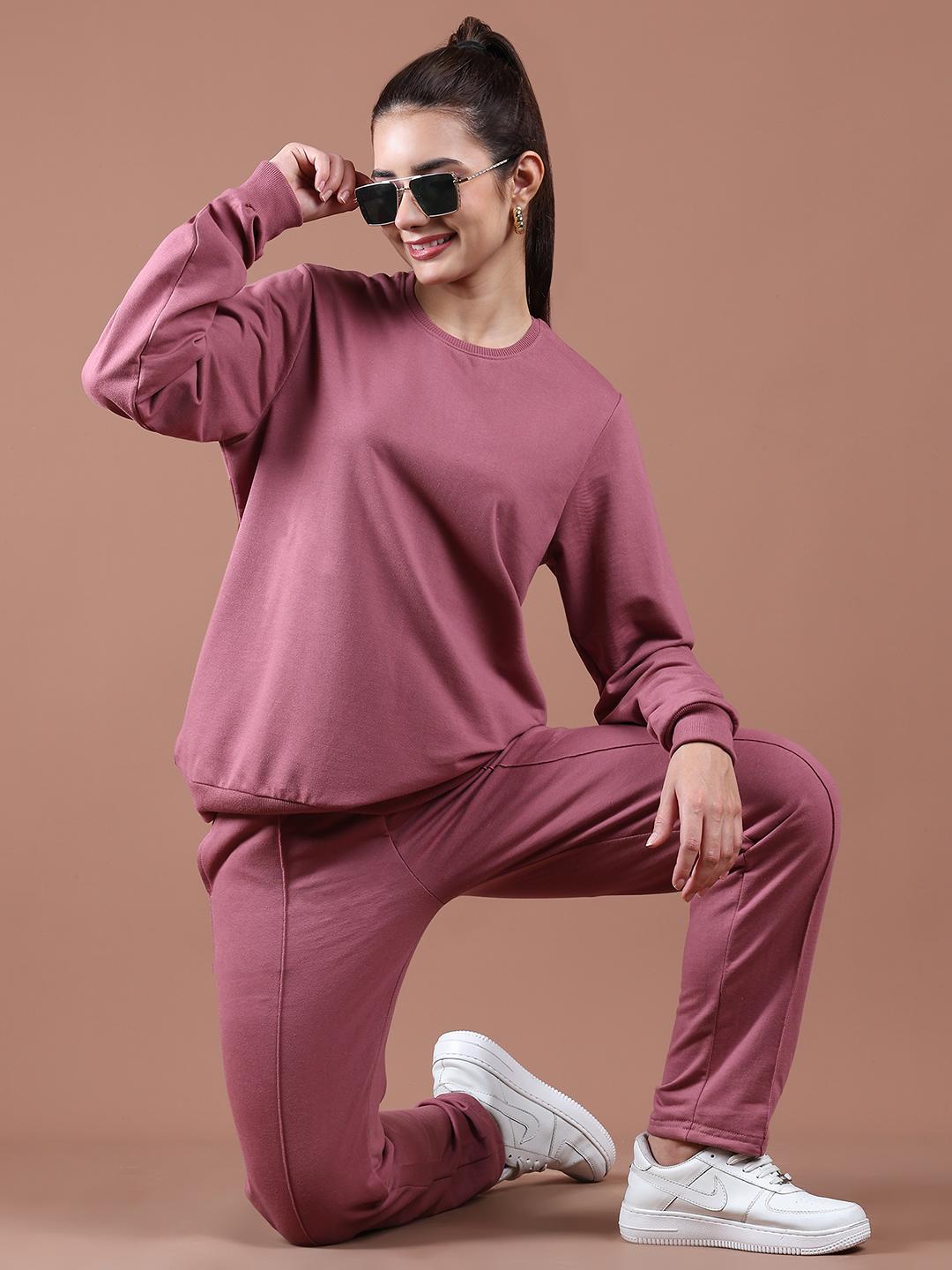 Woman wearing a dusty pink tracksuit and white sneakers on a brown background